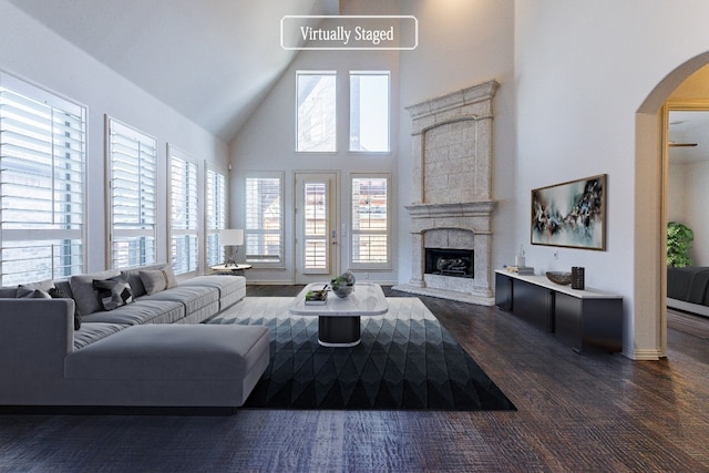 living room featuring high vaulted ceiling, a healthy amount of sunlight, a stone fireplace, and dark hardwood / wood-style floors