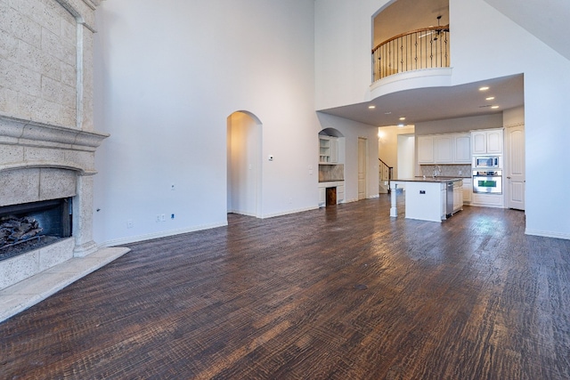 unfurnished living room featuring a towering ceiling, sink, a tile fireplace, and dark hardwood / wood-style floors