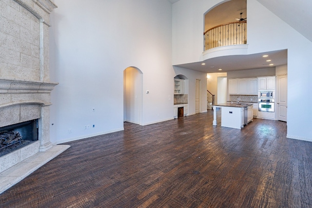 unfurnished living room featuring ceiling fan, a towering ceiling, sink, a tile fireplace, and dark hardwood / wood-style floors