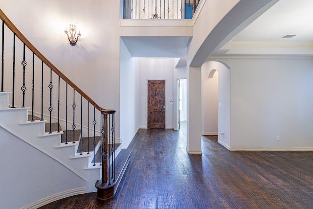 foyer entrance featuring dark wood-type flooring, a towering ceiling, and crown molding