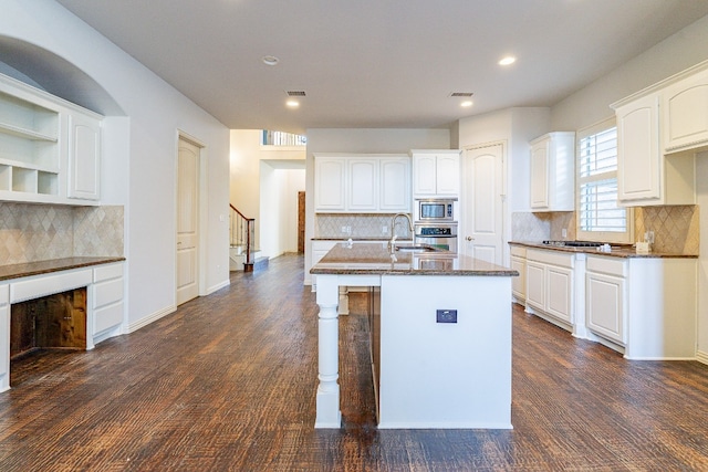 kitchen with appliances with stainless steel finishes, dark wood-type flooring, backsplash, a center island with sink, and white cabinets