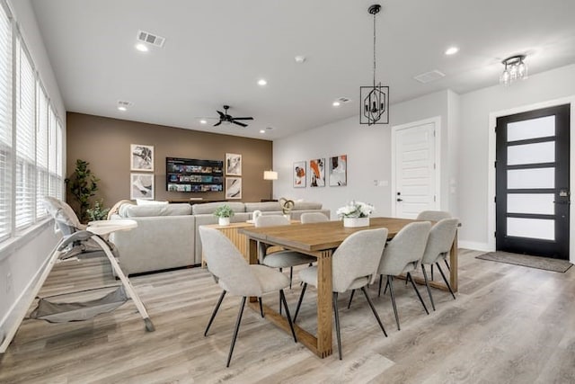 dining space with ceiling fan with notable chandelier and light hardwood / wood-style flooring