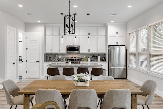 kitchen featuring appliances with stainless steel finishes, hanging light fixtures, white cabinetry, a chandelier, and a kitchen island with sink