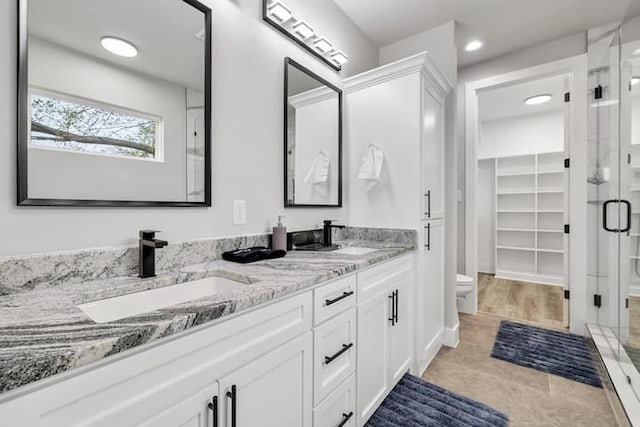 bathroom featuring tile floors, toilet, a shower with door, and dual bowl vanity