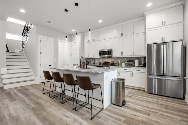 kitchen featuring a kitchen island with sink, pendant lighting, appliances with stainless steel finishes, light hardwood / wood-style floors, and white cabinetry