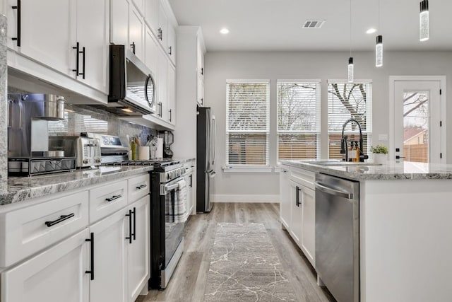 kitchen featuring white cabinets, light hardwood / wood-style flooring, stainless steel appliances, light stone countertops, and decorative light fixtures