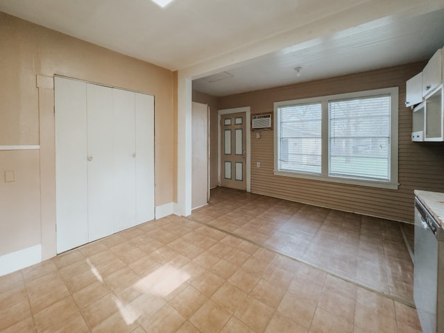 interior space with stainless steel dishwasher, an AC wall unit, and white cabinetry