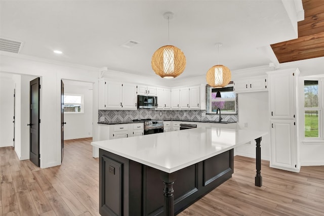 kitchen with hanging light fixtures, backsplash, appliances with stainless steel finishes, light wood-type flooring, and a breakfast bar area