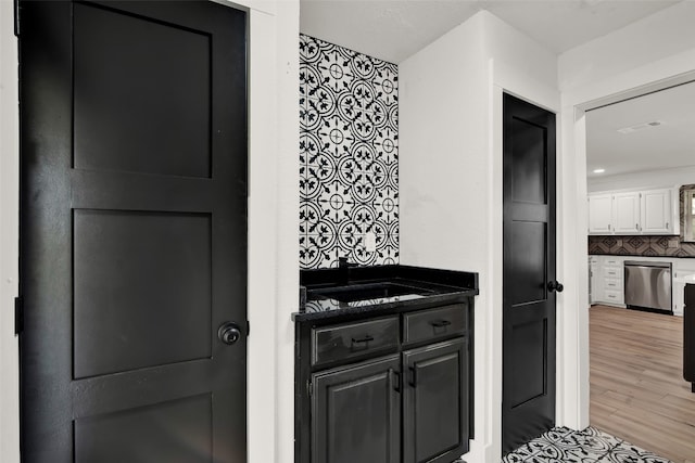 interior space with stainless steel dishwasher, tasteful backsplash, white cabinets, light wood-type flooring, and sink