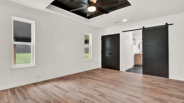 unfurnished bedroom with a barn door, light hardwood / wood-style floors, ensuite bathroom, and multiple windows