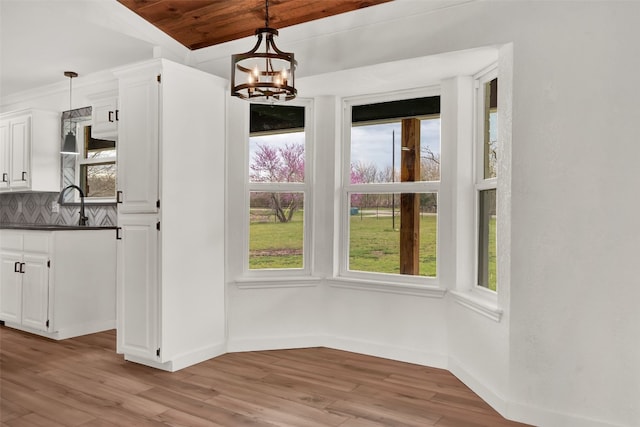 unfurnished dining area with an inviting chandelier, wooden ceiling, and light hardwood / wood-style flooring