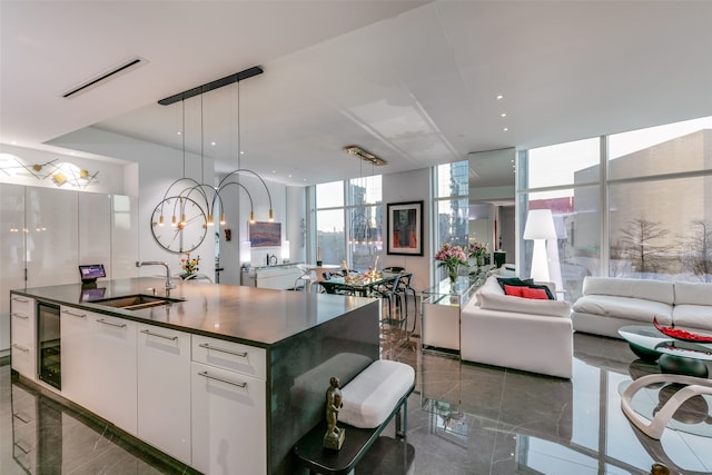 kitchen featuring sink, hanging light fixtures, a kitchen island with sink, a notable chandelier, and white cabinets