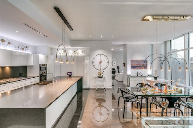 kitchen featuring a large island, stainless steel double oven, decorative light fixtures, and white cabinets