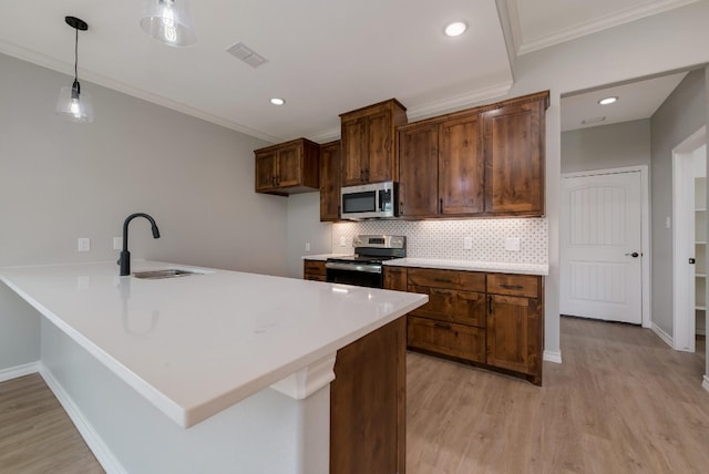 kitchen with decorative light fixtures, stainless steel appliances, light wood-type flooring, backsplash, and sink