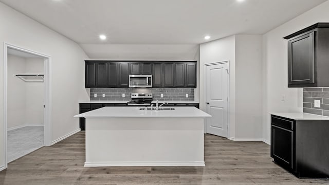 kitchen with light hardwood / wood-style floors, appliances with stainless steel finishes, a kitchen island with sink, and sink