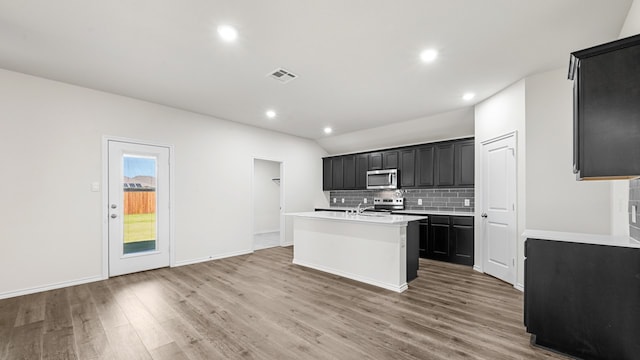 kitchen featuring wood-type flooring, a center island with sink, appliances with stainless steel finishes, and tasteful backsplash