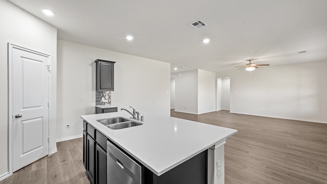 kitchen with light wood-type flooring, ceiling fan, a center island with sink, stainless steel dishwasher, and sink