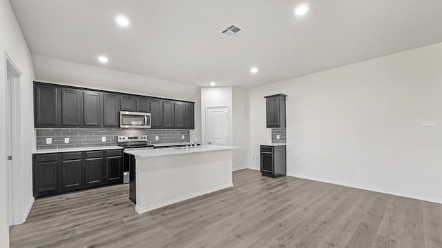 kitchen with appliances with stainless steel finishes, an island with sink, backsplash, light wood-type flooring, and sink