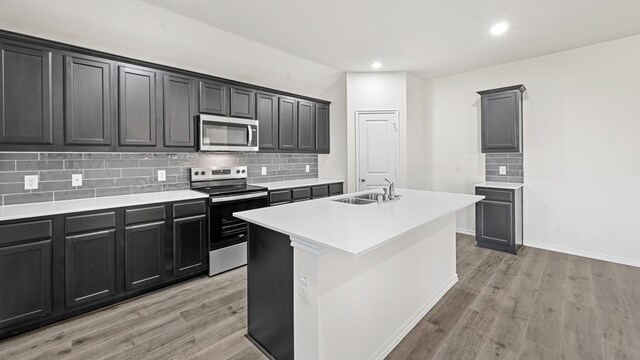 kitchen featuring an island with sink, stainless steel appliances, light wood-type flooring, and tasteful backsplash