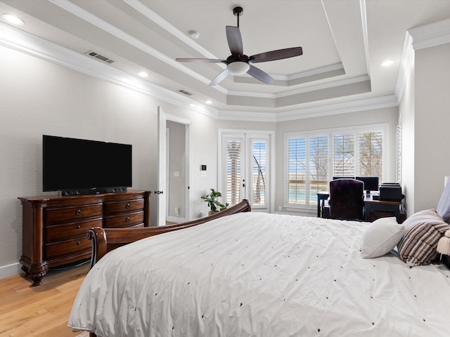 bedroom featuring light wood finished floors, a tray ceiling, ornamental molding, and visible vents