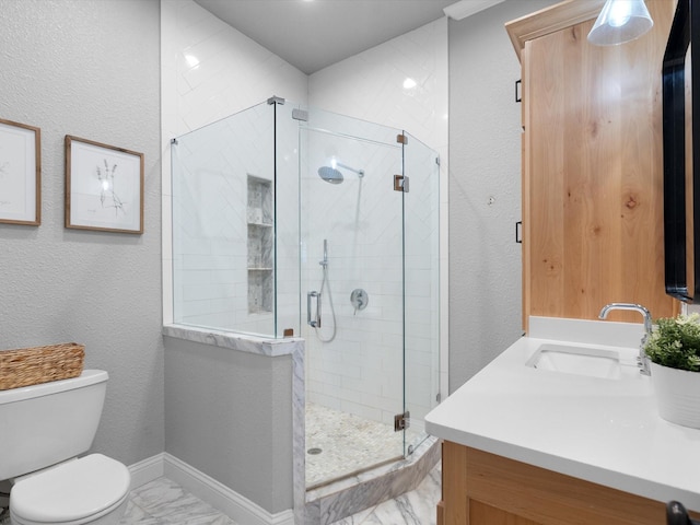 bathroom featuring marble finish floor, a textured wall, toilet, a stall shower, and vanity