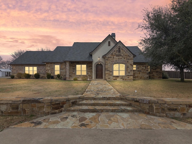 view of front of home featuring stone siding, a lawn, a chimney, and fence