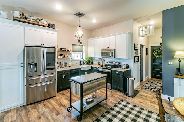 kitchen with decorative backsplash, light wood-type flooring, stainless steel appliances, sink, and hanging light fixtures