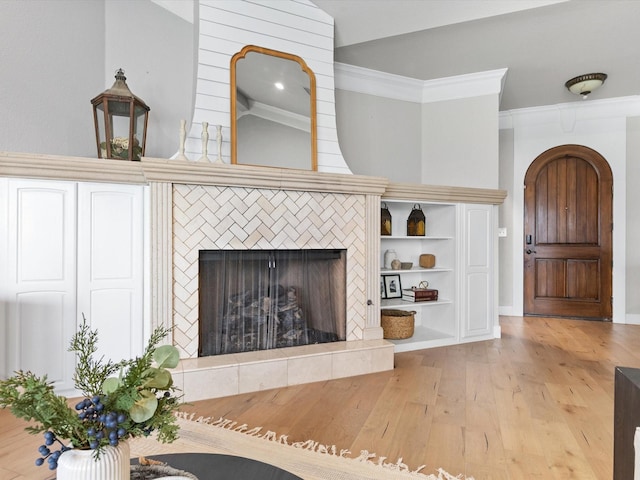 unfurnished living room featuring a tiled fireplace, light hardwood / wood-style flooring, ornamental molding, and vaulted ceiling