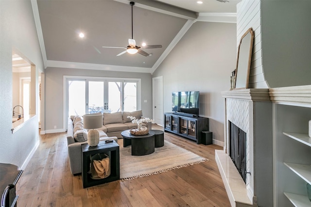 living room featuring a tiled fireplace, ceiling fan, lofted ceiling with beams, and light wood-type flooring