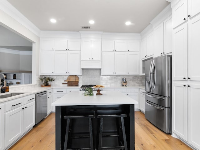 kitchen with white cabinets, appliances with stainless steel finishes, a center island, light countertops, and a sink