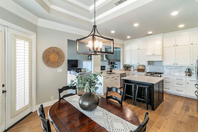 dining room featuring a raised ceiling, sink, crown molding, light hardwood / wood-style floors, and a chandelier