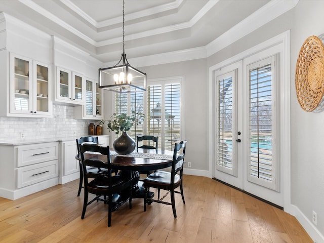 dining space featuring a chandelier, french doors, a tray ceiling, light wood finished floors, and crown molding