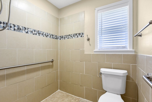 bathroom with toilet, a tile shower, tile walls, and a wealth of natural light