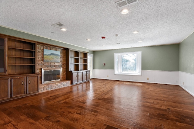 unfurnished living room featuring brick wall, a brick fireplace, built in features, dark wood-type flooring, and a textured ceiling