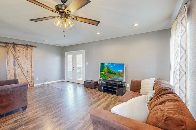 living room with wood-type flooring, a barn door, ceiling fan, and french doors