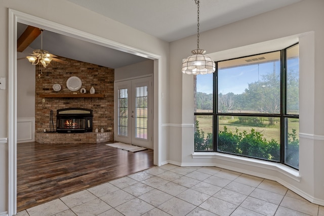 unfurnished living room with a fireplace, ceiling fan, lofted ceiling with beams, french doors, and light tile patterned floors