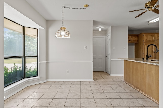 kitchen featuring light tile patterned flooring, ceiling fan, hanging light fixtures, sink, and light stone counters