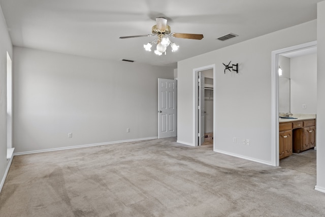 unfurnished bedroom with a spacious closet, ensuite bath, light colored carpet, and ceiling fan