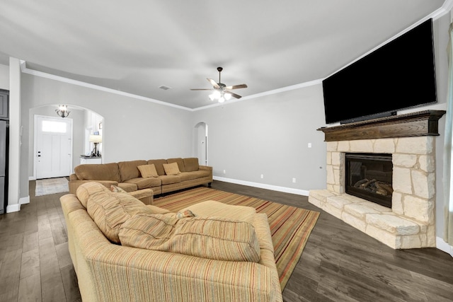 living room with ornamental molding, ceiling fan, dark wood-type flooring, and a stone fireplace