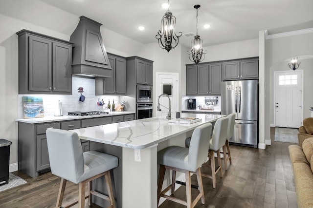 kitchen featuring light stone countertops, appliances with stainless steel finishes, custom range hood, dark hardwood / wood-style flooring, and pendant lighting