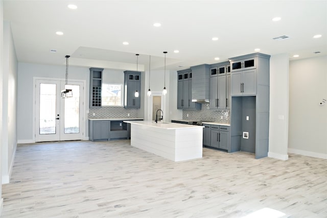 kitchen with an island with sink, light hardwood / wood-style floors, tasteful backsplash, and pendant lighting