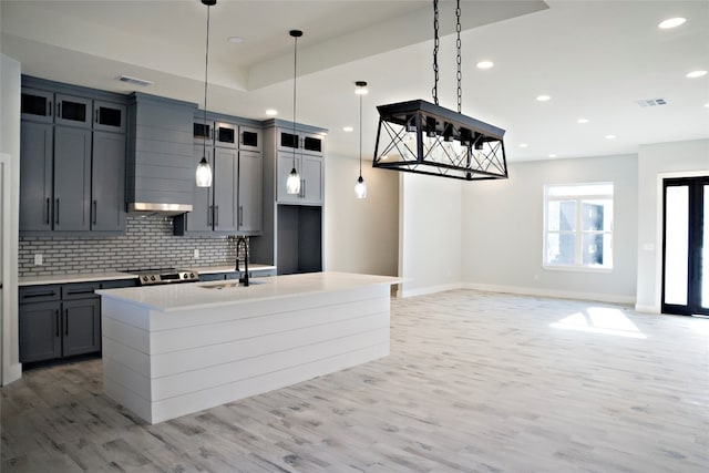 kitchen featuring light hardwood / wood-style floors, sink, tasteful backsplash, and a kitchen island with sink