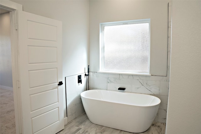 bathroom with hardwood / wood-style floors, a tub, and tile walls