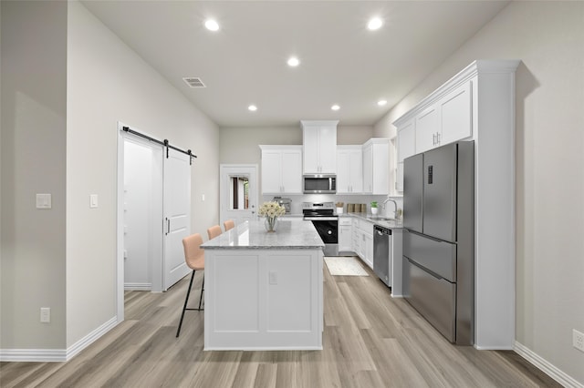 kitchen with light stone counters, white cabinetry, stainless steel appliances, a center island, and a barn door