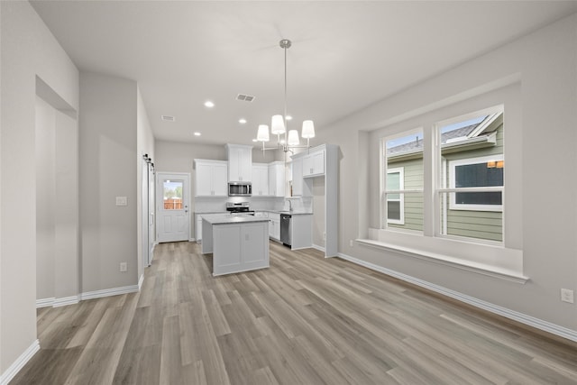 kitchen with white cabinetry, a kitchen island, stainless steel appliances, light wood-type flooring, and decorative light fixtures