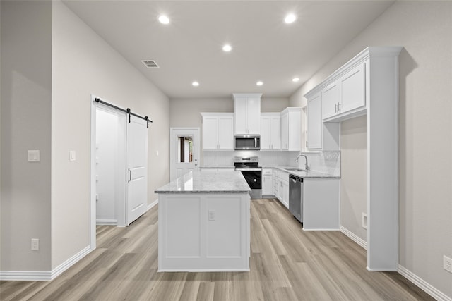 kitchen with white cabinets, a kitchen island, a barn door, appliances with stainless steel finishes, and light stone countertops