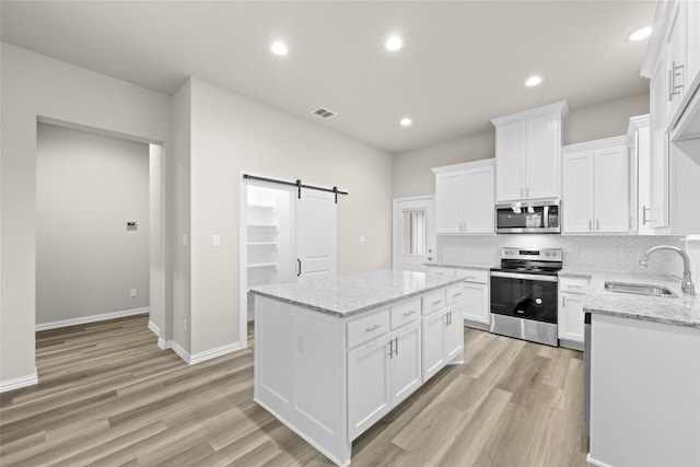 kitchen featuring a barn door, white cabinetry, a center island, and stainless steel appliances