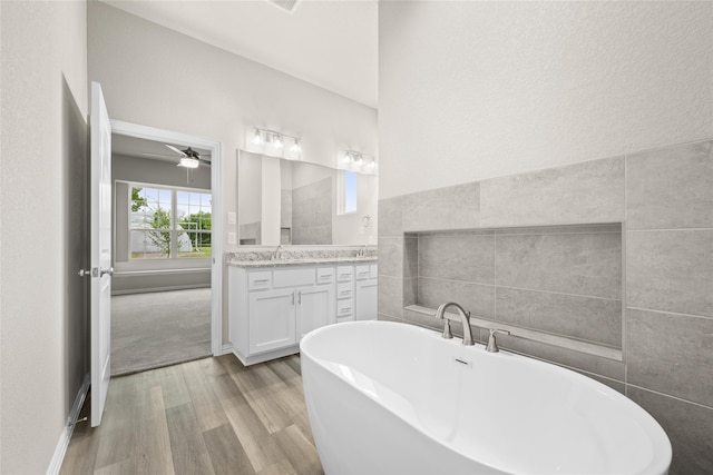 bathroom with tile walls, a washtub, hardwood / wood-style floors, ceiling fan, and vanity