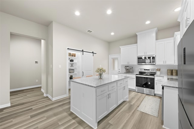 kitchen with light stone counters, appliances with stainless steel finishes, a barn door, and white cabinetry