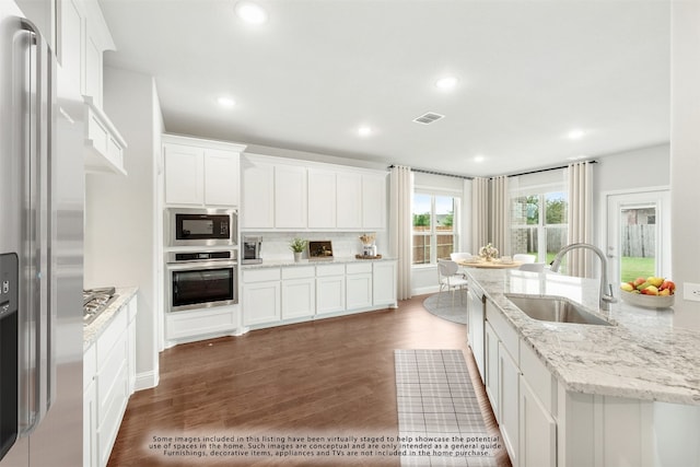 kitchen with light stone countertops, white cabinetry, stainless steel appliances, and dark wood-type flooring